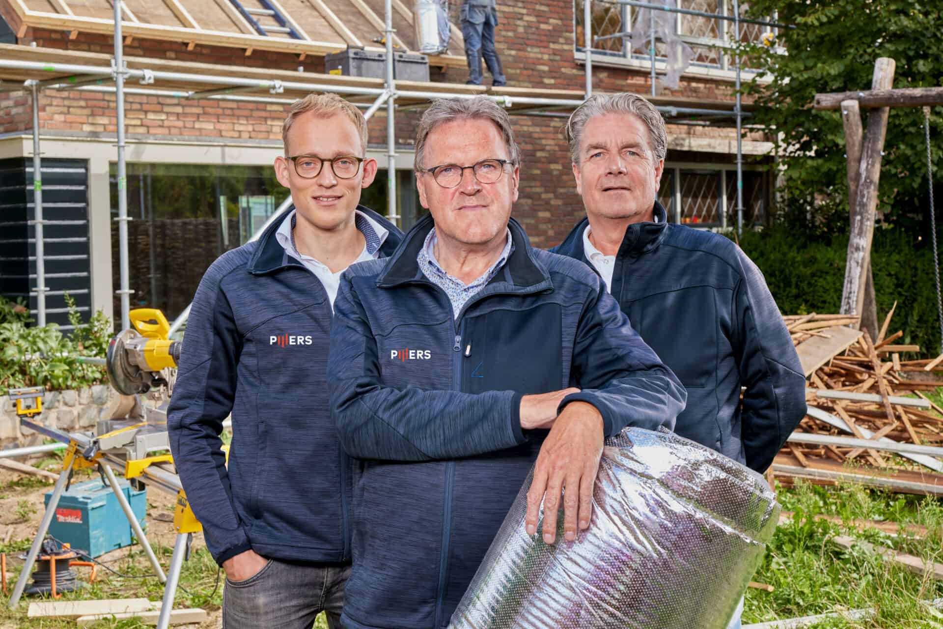 Driest personen in werkkleding met Pijlers logo, bouwproces op achtergrond.